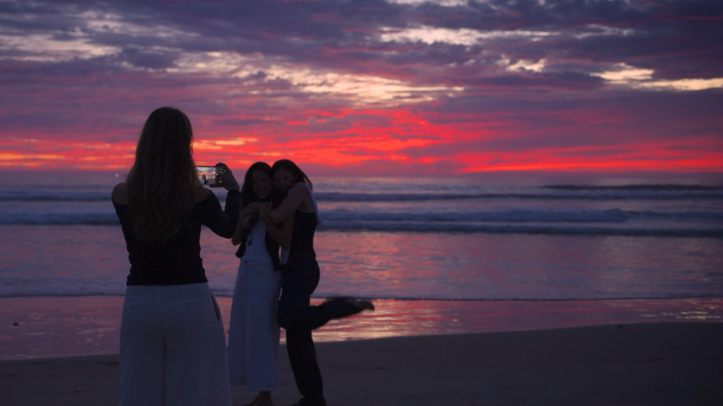 Friends at the shoreline at sunset, one taking a photo