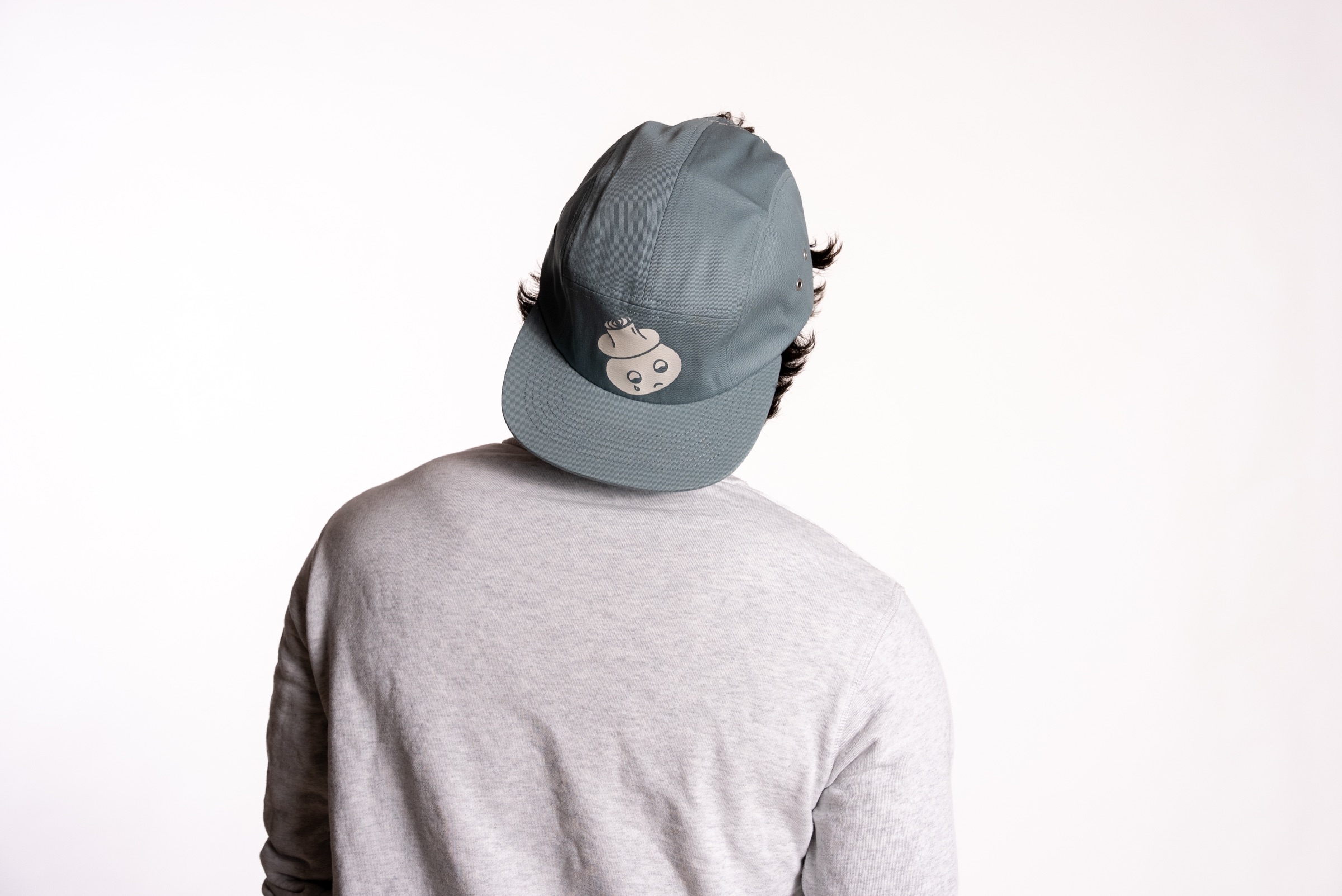 A man in a grey Boys Don't Cry cap, seen from behind
